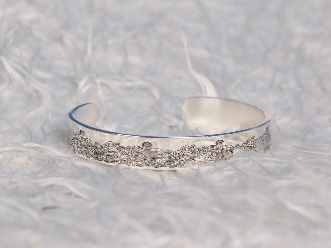 The image displays the "I AM THE STORM NEW" bracelet. The bracelet is made of titanium steel with 316L stainless silver plating, ensuring durability and resistance to fading, tarnishing, and corrosion. It features the inscription "I AM THE STORM NEW" on the inside. The bracelet has a diameter of 2.5 inches, a length of 6.2 inches, and a width of 3/8 inch, with adjustable openings to fit most wrists. The package includes a gift card, a gift bouquet, and a velvet bag for presentation.