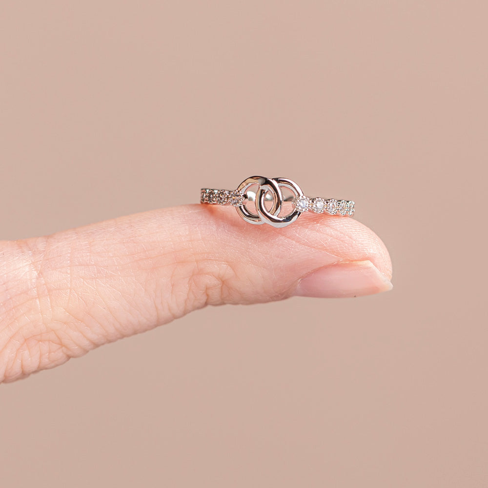 The photo shows a single 'To My Daughter Forever linked' Interlocking Ring on the finger of a hand, but not worn, just placed on the finger. This ring features two interlocking circular designs, symbolizing the unbreakable bond between mother and daughter. The set includes the ring, a greeting card, a gift box and a gift bag to hold it all. Material: S925 sterling silver, processing technique: plated. 