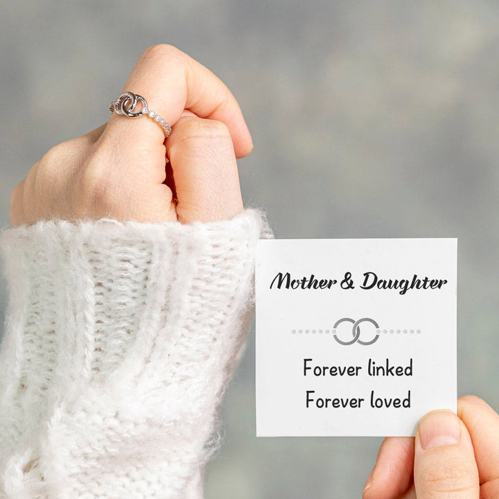 Pictured is the [Parent-Child Set] To My Daughter "Forever linked" Interlocking Ring in S925 sterling silver with platinum plating, worn on one hand while the other hand holds a greeting card.